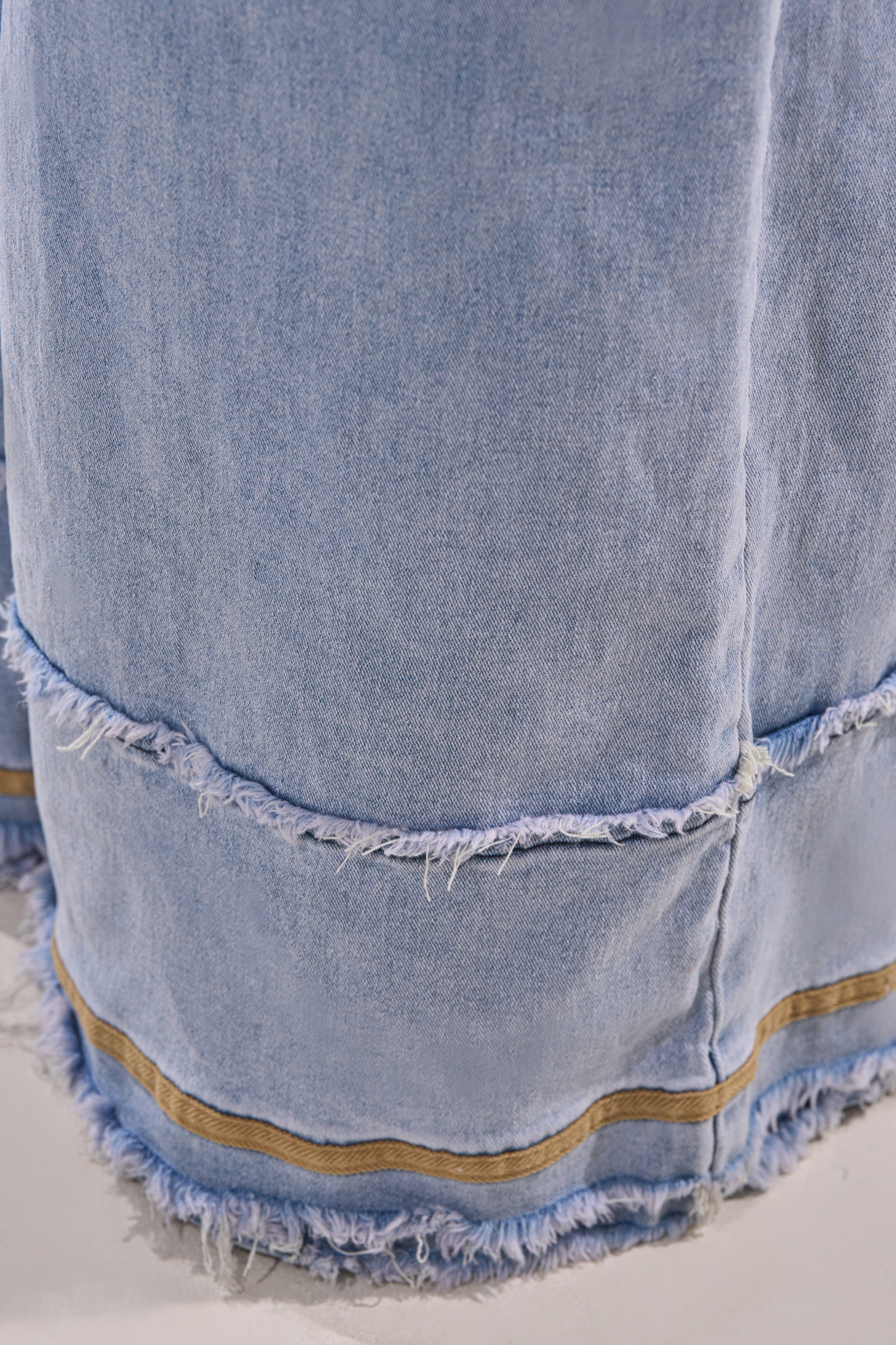 Close-up of light-wash denim fabric with visible seams, frayed edges, and two brownish-gold stripes near the hem highlights the texture and relaxed style of the AT LEAST I LOOK CUTE DENIM JUMPSUIT. 8