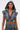 A woman wears the DOWN AND DIRTY DENIM HOODED VEST with matching camo high-waisted pants and hoop earrings, standing confidently against a plain light background. Tattoos decorate her arm.