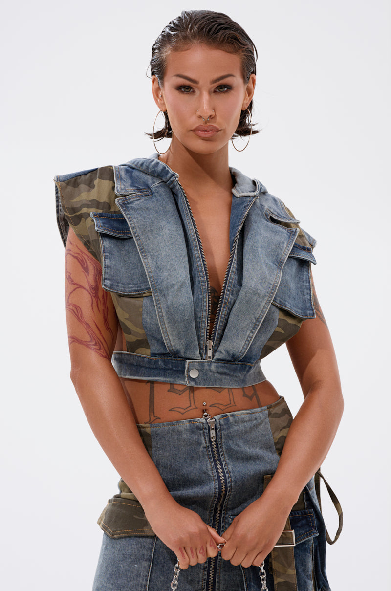 A person with wet, slicked-back hair styles the DOWN AND DIRTY DENIM HOODED VEST and matching skirt. Large pockets, visible arm tattoos, and a confident expression complete their edgy look. 1