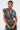 A person with wet, slicked-back hair styles the DOWN AND DIRTY DENIM HOODED VEST and matching skirt. Large pockets, visible arm tattoos, and a confident expression complete their edgy look.