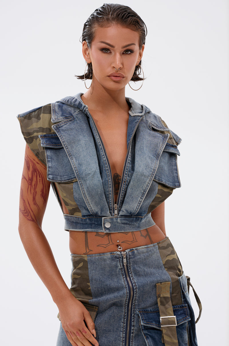 A person with wet, slicked-back hair wears the DOWN AND DIRTY DENIM HOODED VEST with camouflage accents and a zip front, paired with a matching high-waisted skirt featuring zippers and camo panels. 2