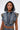 A woman with hoop earrings and facial piercings poses confidently against a plain, light background wearing the DOWN AND DIRTY DENIM HOODED VEST featuring camo details.
