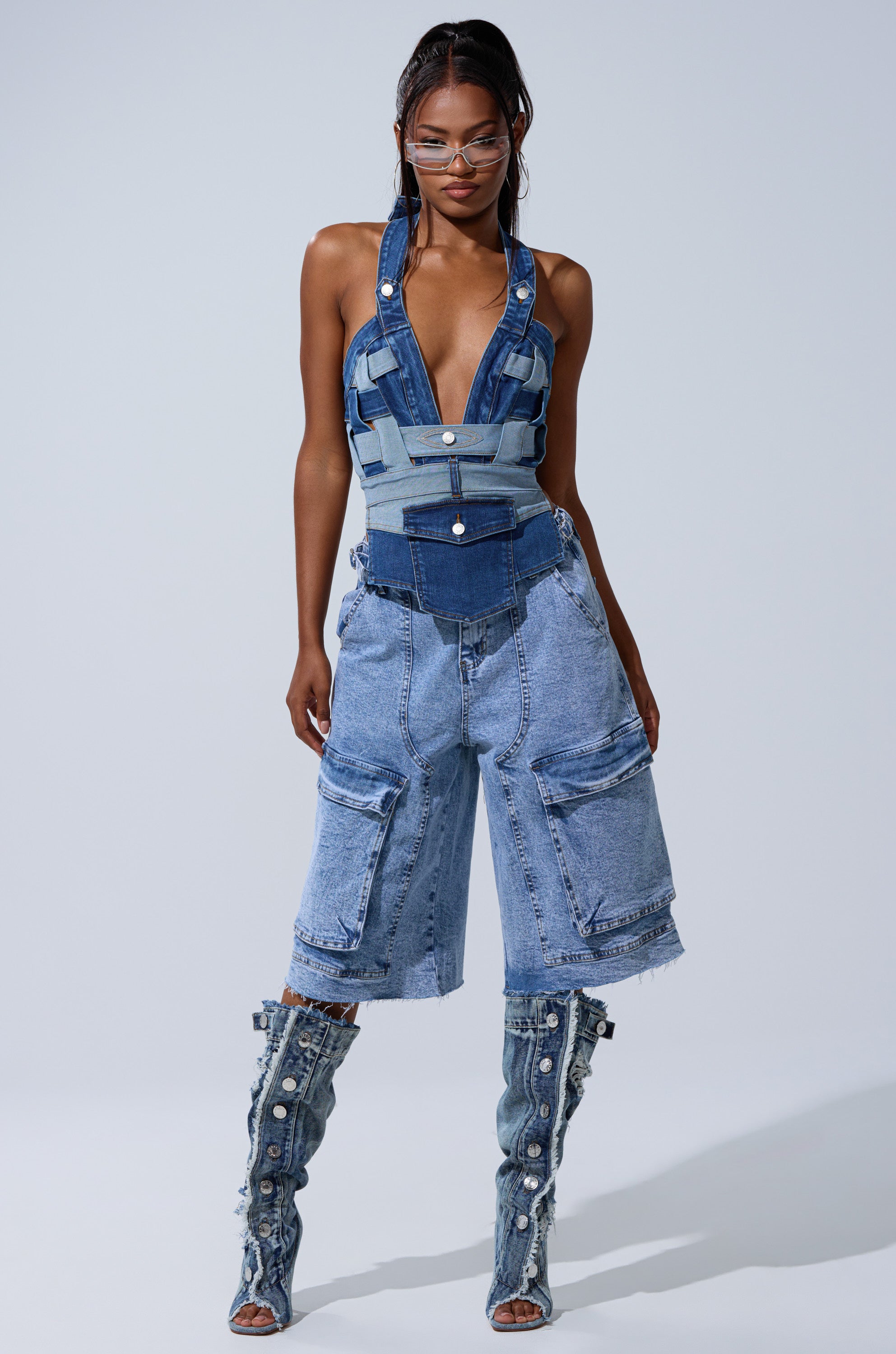 A woman wears the CATCH ME ABSTRACT DENIM CORSET with high-waisted loose denim shorts, knee-high buttoned denim boots, styled-back hair, and glasses. 5