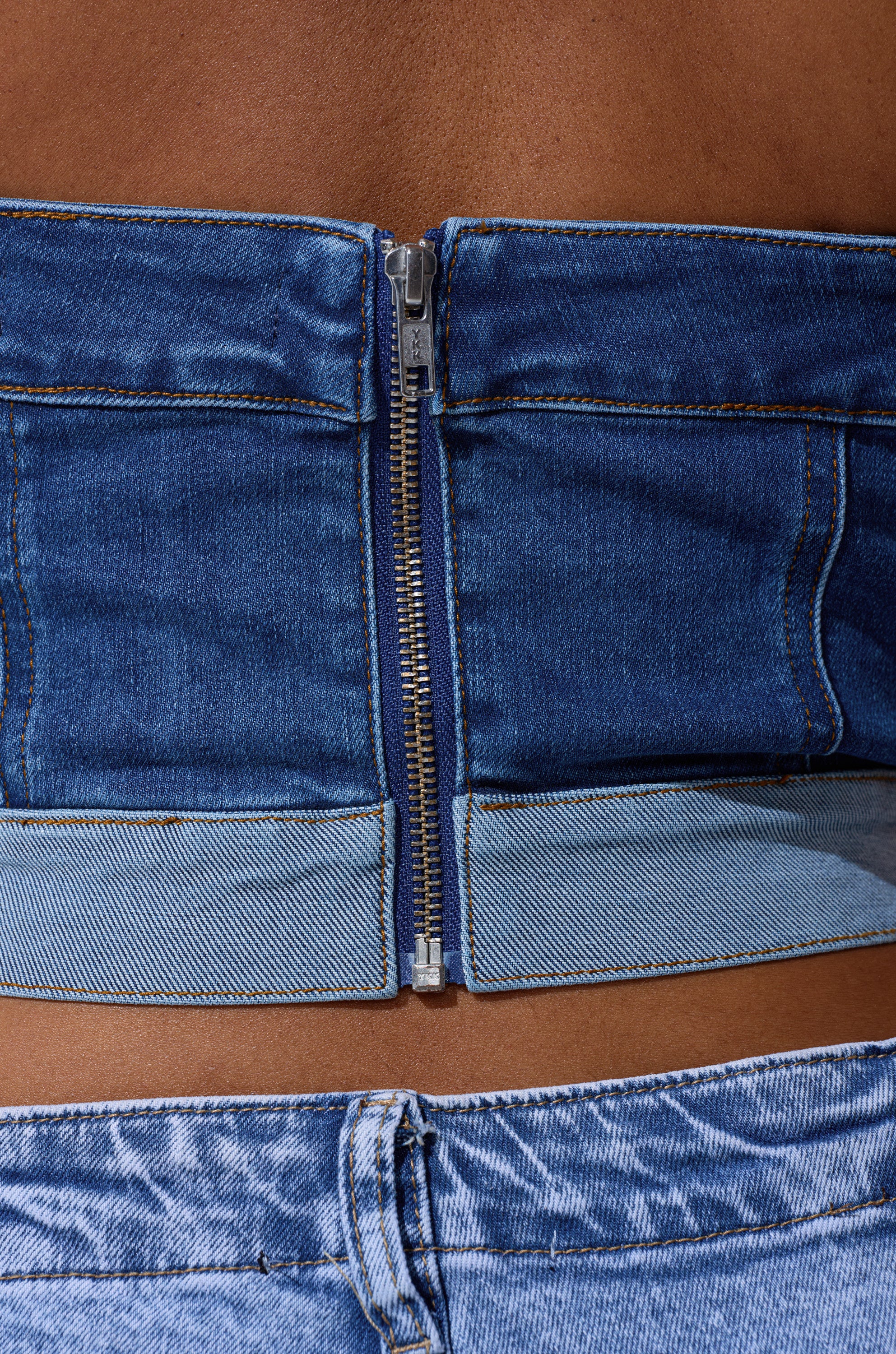 Close-up of a lower back wearing the CATCH ME ABSTRACT DENIM CORSET with a visible zipper, styled with light blue jeans. Bare skin above the waistband highlights a chic denim-on-denim look. 6