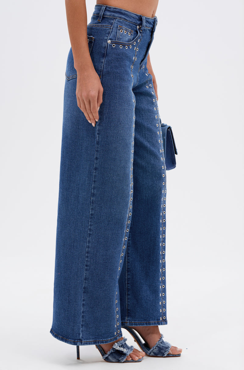 Someone in SOFIA RELAXED DENIM WITH GROMMET, styled with high-heeled frayed denim sandals and holding a small clutch bag.