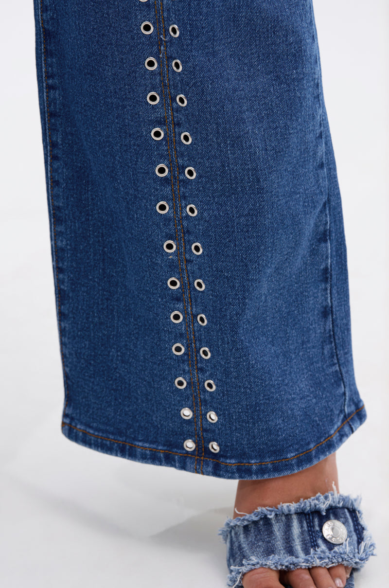 A close-up of the SOFIA RELAXED DENIM WITH GROMMET featuring silver grommets and a frayed hem, paired with an open-toe sandal with a frayed denim strap and a large silver button.