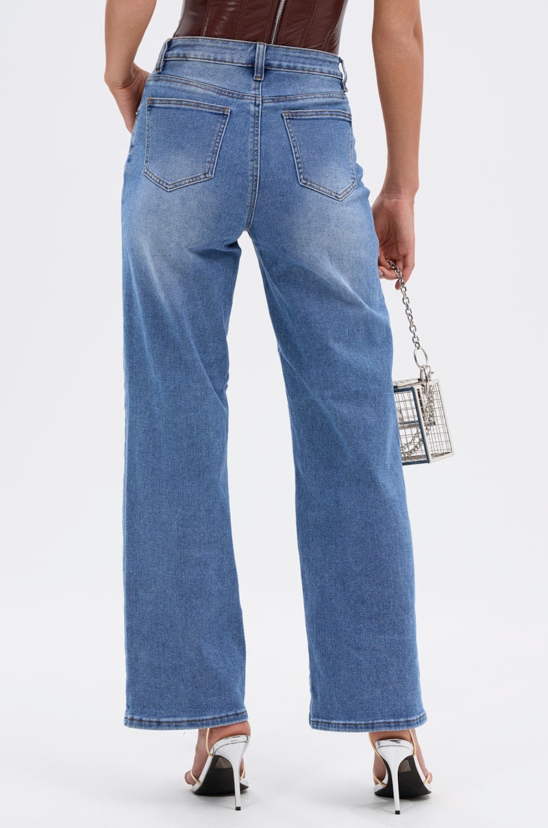 Wearing SNAP OUT OF IT DENIM PANT in blue, a brown sleeveless top, white high-heeled sandals, and holding a small silver cage purse, this person is seen from the back. 5