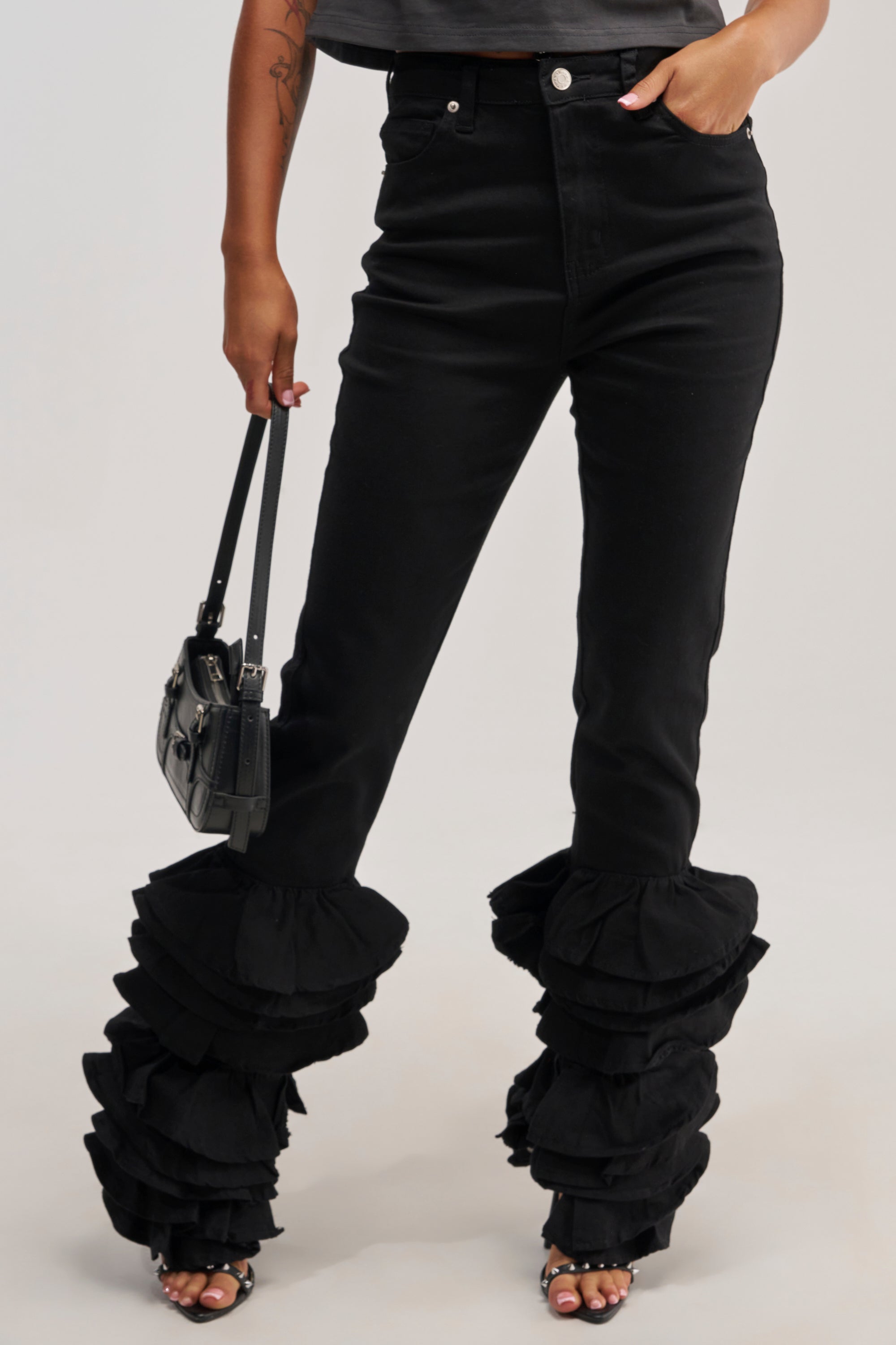 Wearing the NOT ENOUGH RUFFLES DENIM—featuring a high-rise waist and layered ruffles at the ankles—paired with a small black handbag and open-toed heels, makes for the perfect bold statement jeans for a night out.