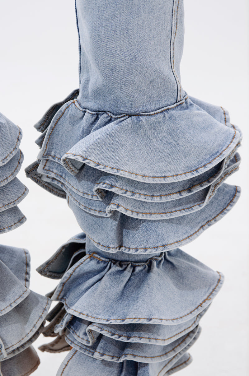 Close-up of NOT ENOUGH RUFFLE DENIM fab­ric in light blue, featuring dramatic tiered flounces stacked at the hem for a textured, voluminous look—perfect for adding statement style to any outfit.