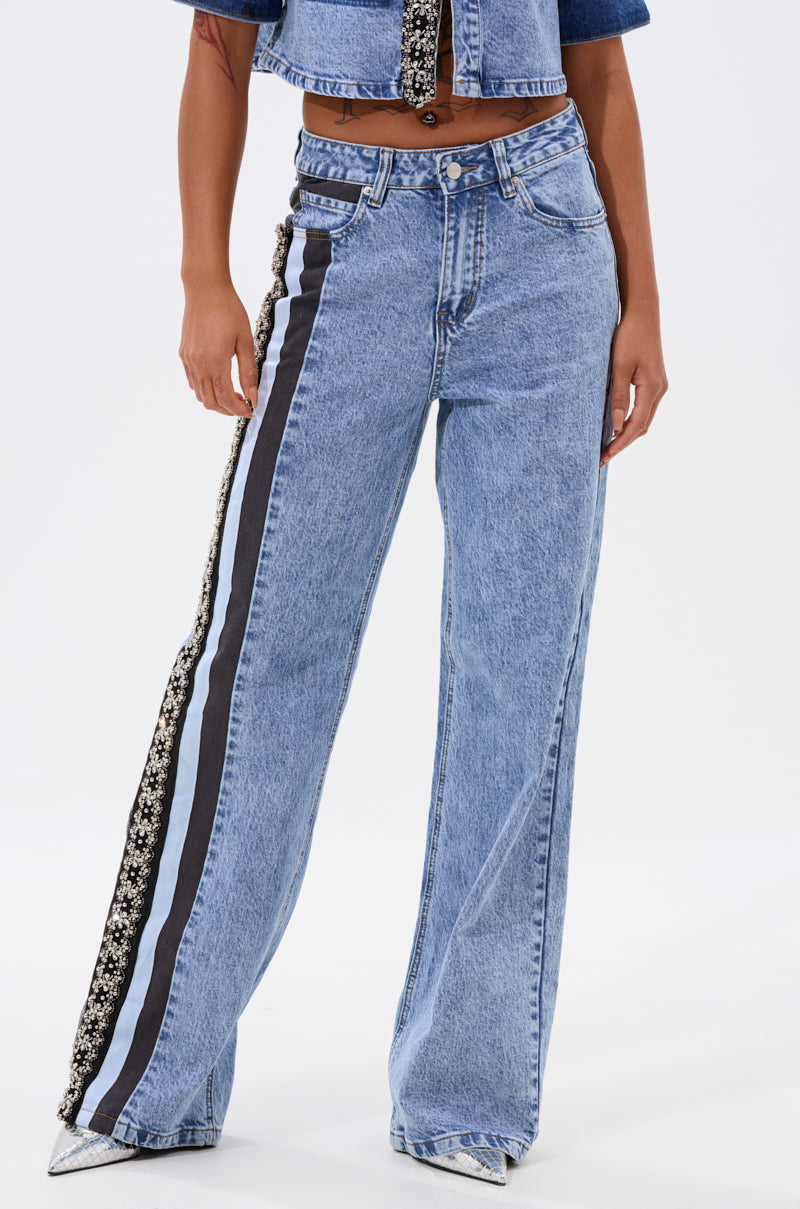 Someone wearing ELEVATED RELAXED DENIM—high-waisted, light-wash wide-leg jeans with black and white side stripes and floral details—paired with a cropped denim jacket and pointed silver shoes. 2