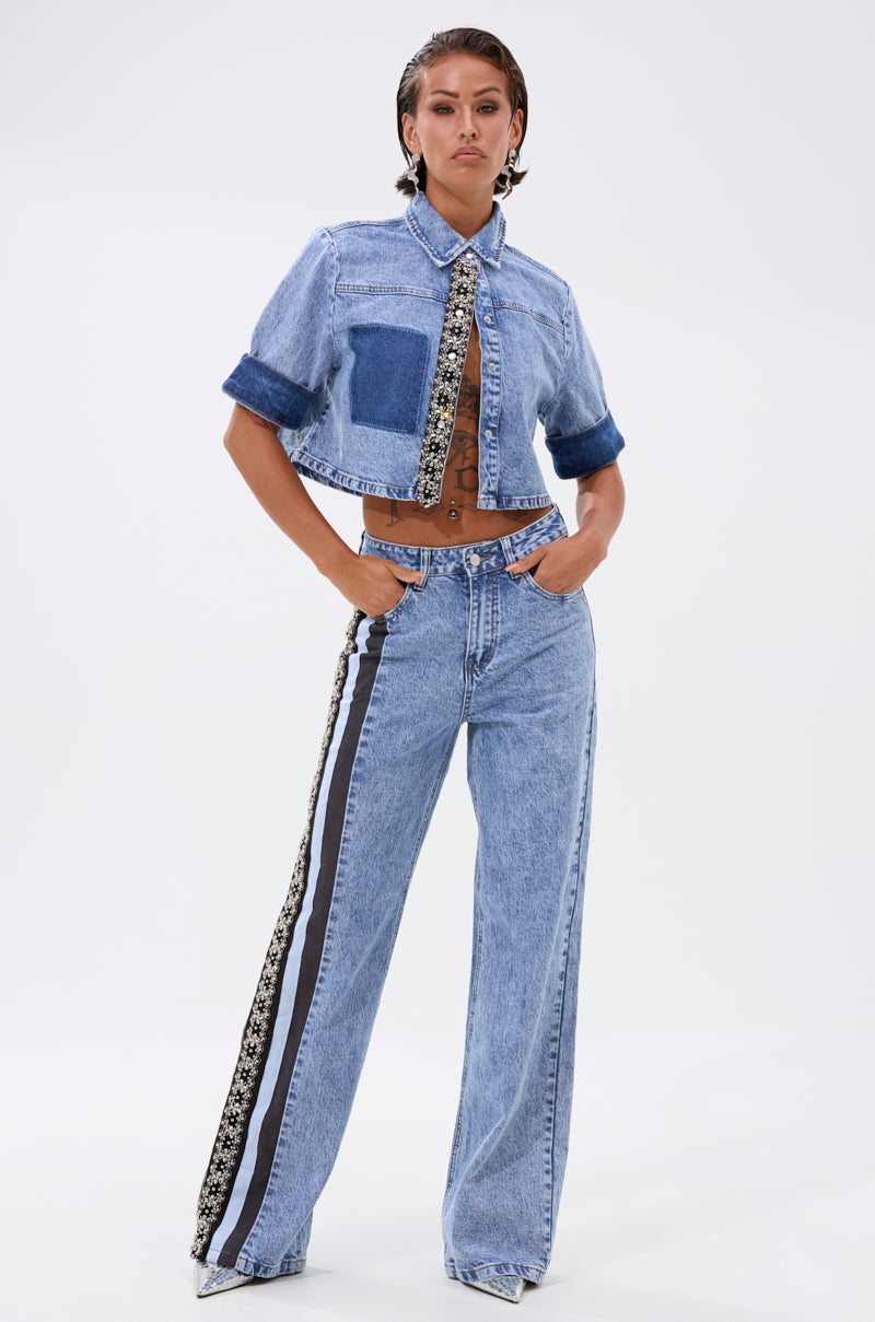 A woman stands confidently against a white background in ELEVATED RELAXED DENIM: a cropped, short-sleeve light-wash denim jacket with patch pocket and high-waisted, wide-leg jeans with black and white side stripes. 6