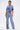 A woman stands confidently in the ELEVATED DENIM BUTTON DOWN, a cropped dual-tone denim shirt paired with high-waisted light blue jeans featuring a black-and-white stripe down one leg and pointed shoes, against a plain white background.