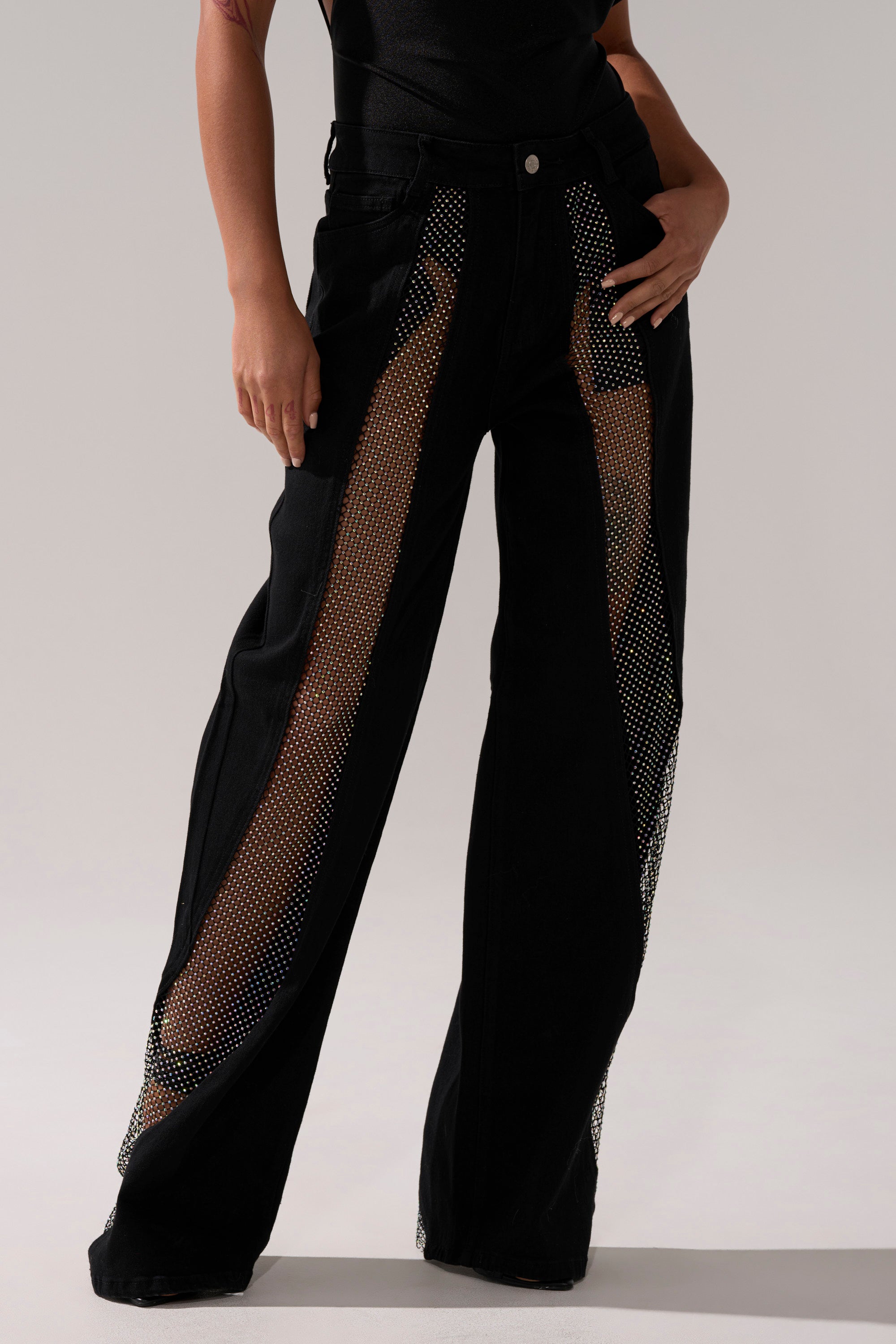 Wearing the SOMETHING DIFFERENT RELAXED DENIM WITH RHINESTONE MESH, featuring black denim with sheer mesh panels and sparkling rhinestone embellishments, paired with a black top; only the lower half is visible.