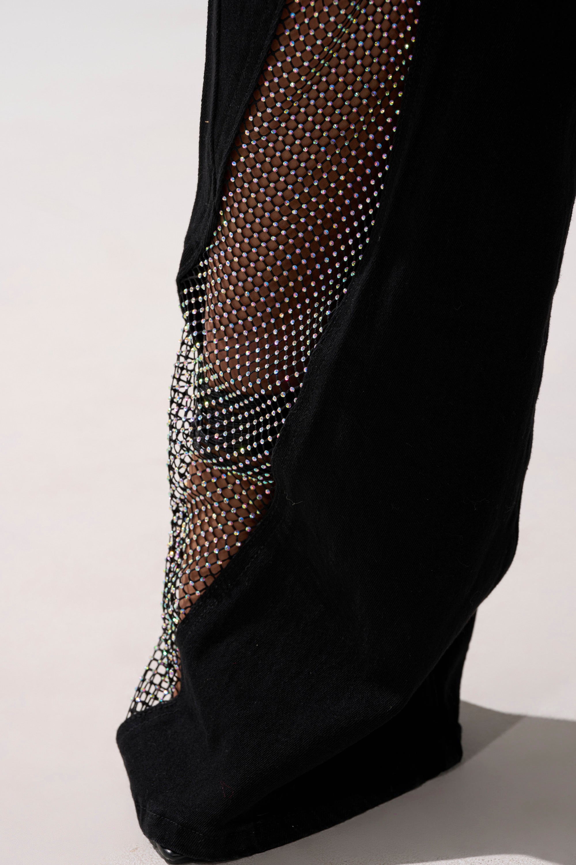 Close-up of the SOMETHING DIFFERENT RELAXED DENIM WITH RHINESTONE MESH, showing the wide-leg jeans’ sheer, sparkling rhinestone mesh panel that reveals skin. The background is a plain, light surface.