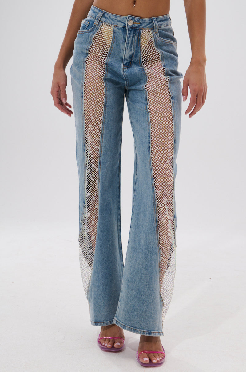 A person models the BLING BLING RELAXED DENIM—high-rise blue jeans with sheer mesh front panels—paired with purple open-toe heels against a plain white background. 0