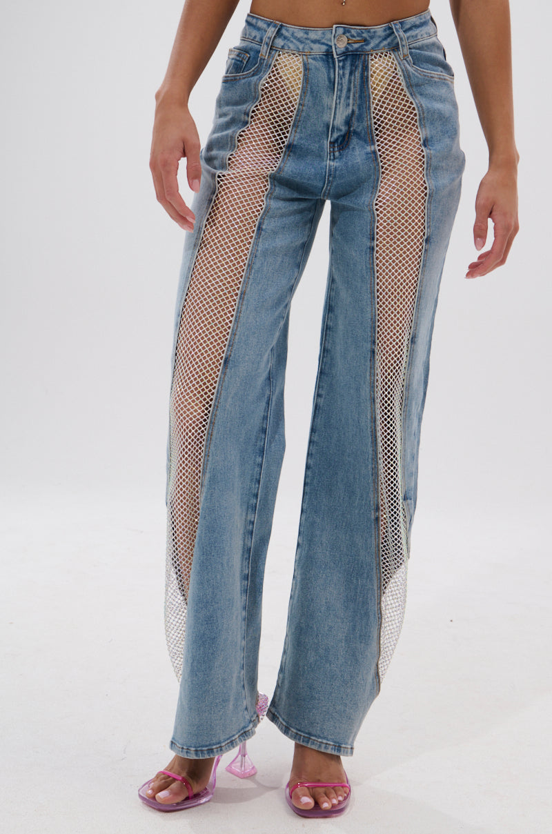 A person models the BLING BLING RELAXED DENIM, featuring high-rise jeans with large mesh cutouts down the front and pink heeled sandals, shown from waist to feet against a plain white background. 2