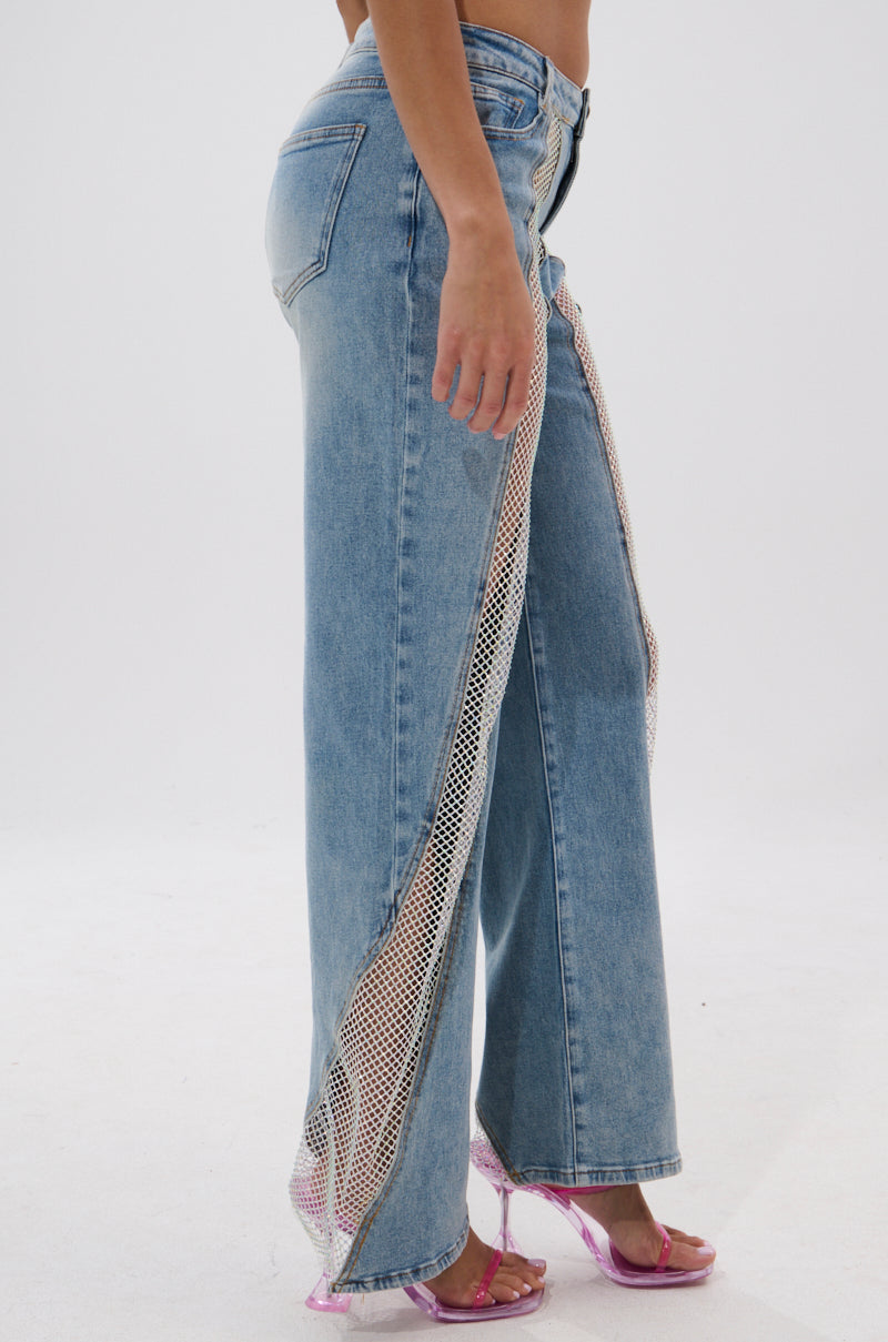 A person wears BLING BLING RELAXED DENIM, featuring high-rise, wide-leg blue jeans with side mesh panels and clear pink heeled sandals, creating a standout relaxed denim look against a plain white background. 3