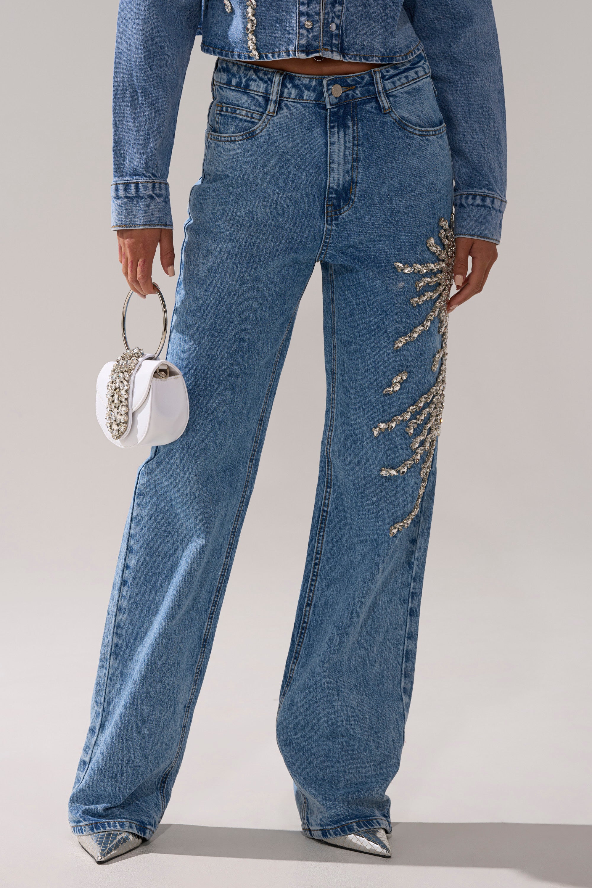 Wearing SPARKLE AND SHINE QUEEN RELAXED DENIM with a matching jacket, pointed metallic shoes, and a small white circular-handle handbag.