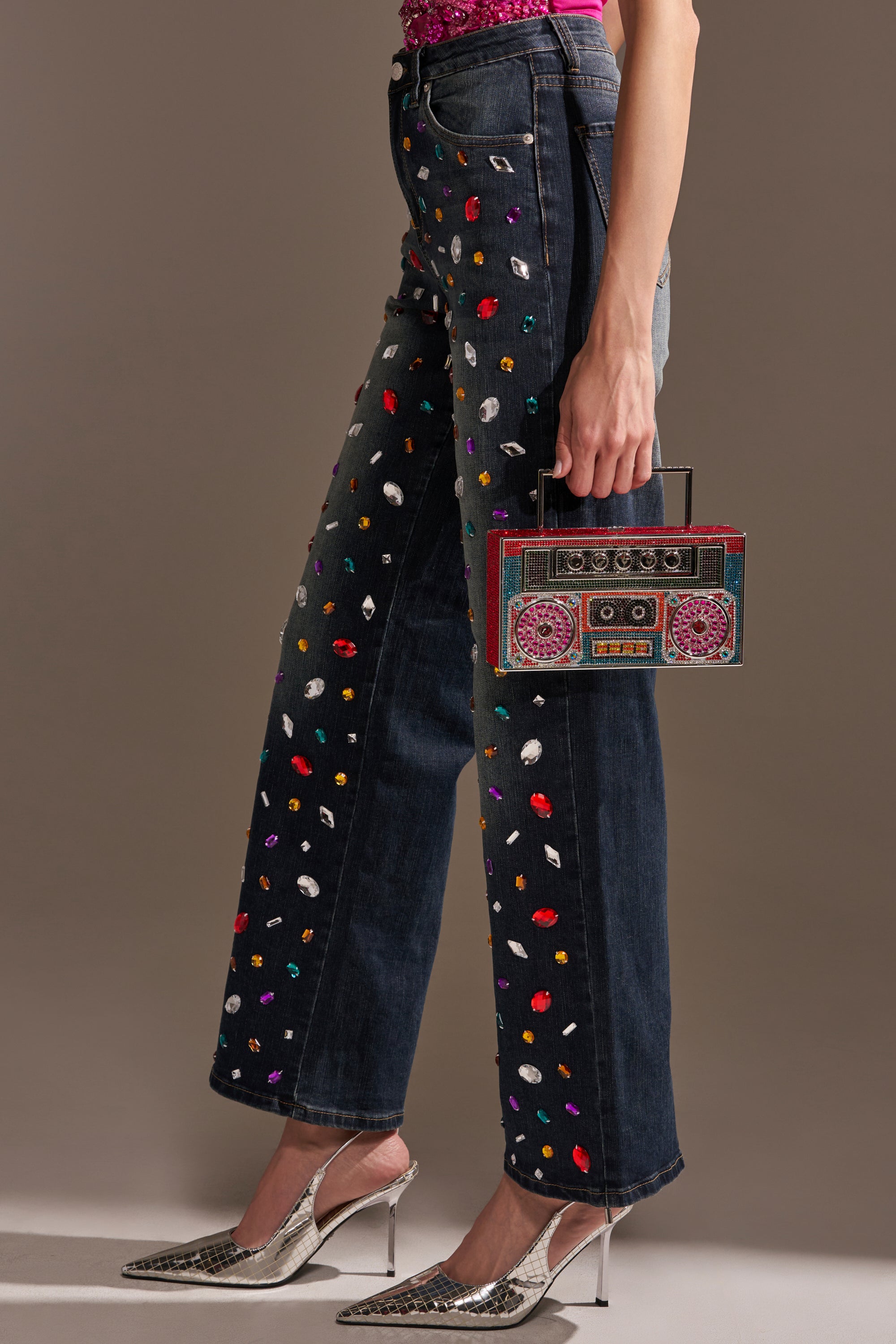 Wearing JEWELERS ROW RHINESTONE DENIM JEANS adorned with bold gems, silver pointed heels, and carrying a vibrant retro boombox-shaped handbag.