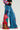 A person sporting the NOT SORRY PATCHWORK DENIM JEANS, adorned with vivid embroidered patches such as cherries and numbers. These jeans, showcasing a wide-leg silhouette, are complemented by a sweater featuring red and blue striped sleeves against a plain light background.