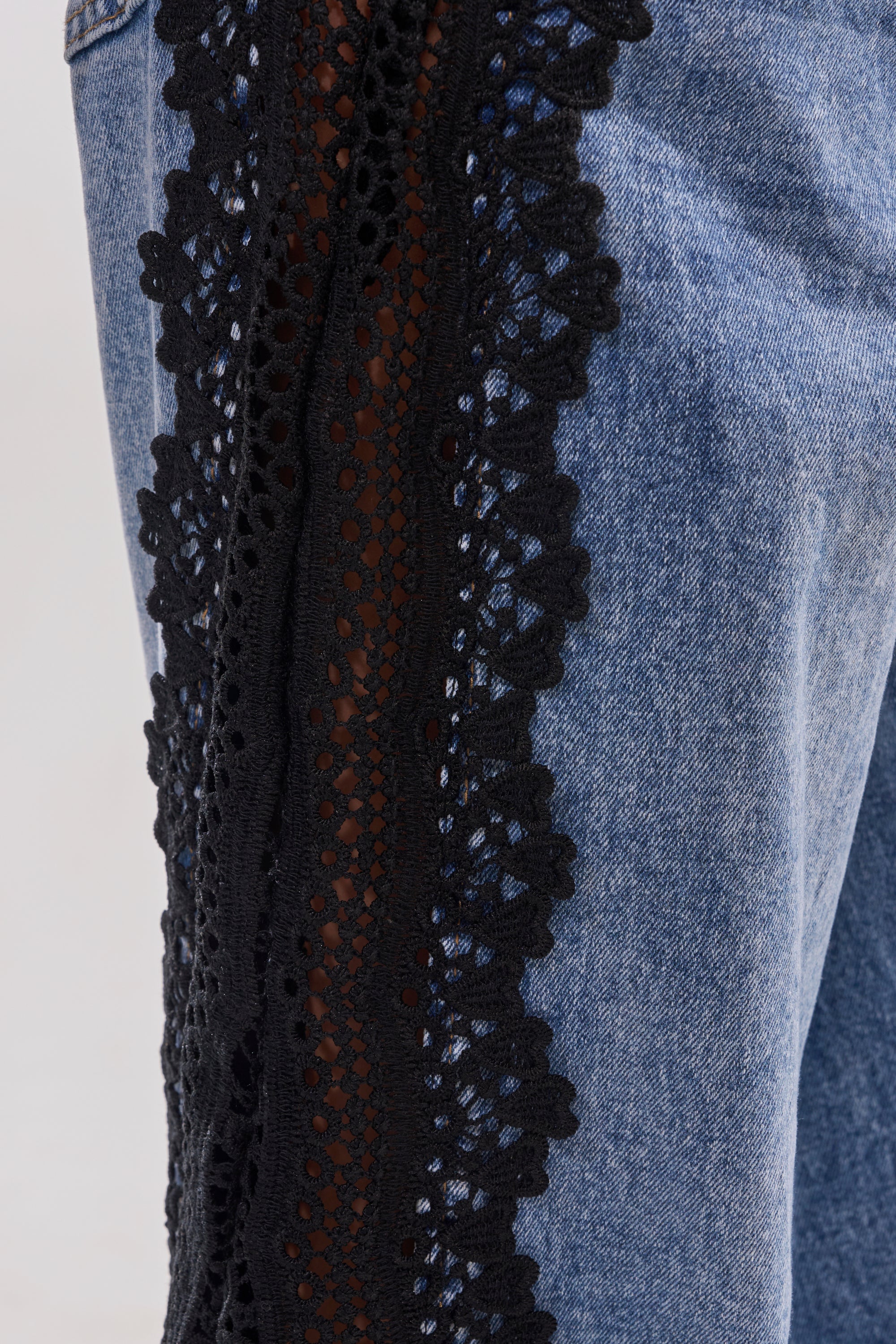 Close-up of the LOCKED IN LACE DENIM wide-leg jeans with a high-rise waist and black floral lace trim running vertically along the outer side seam. 8