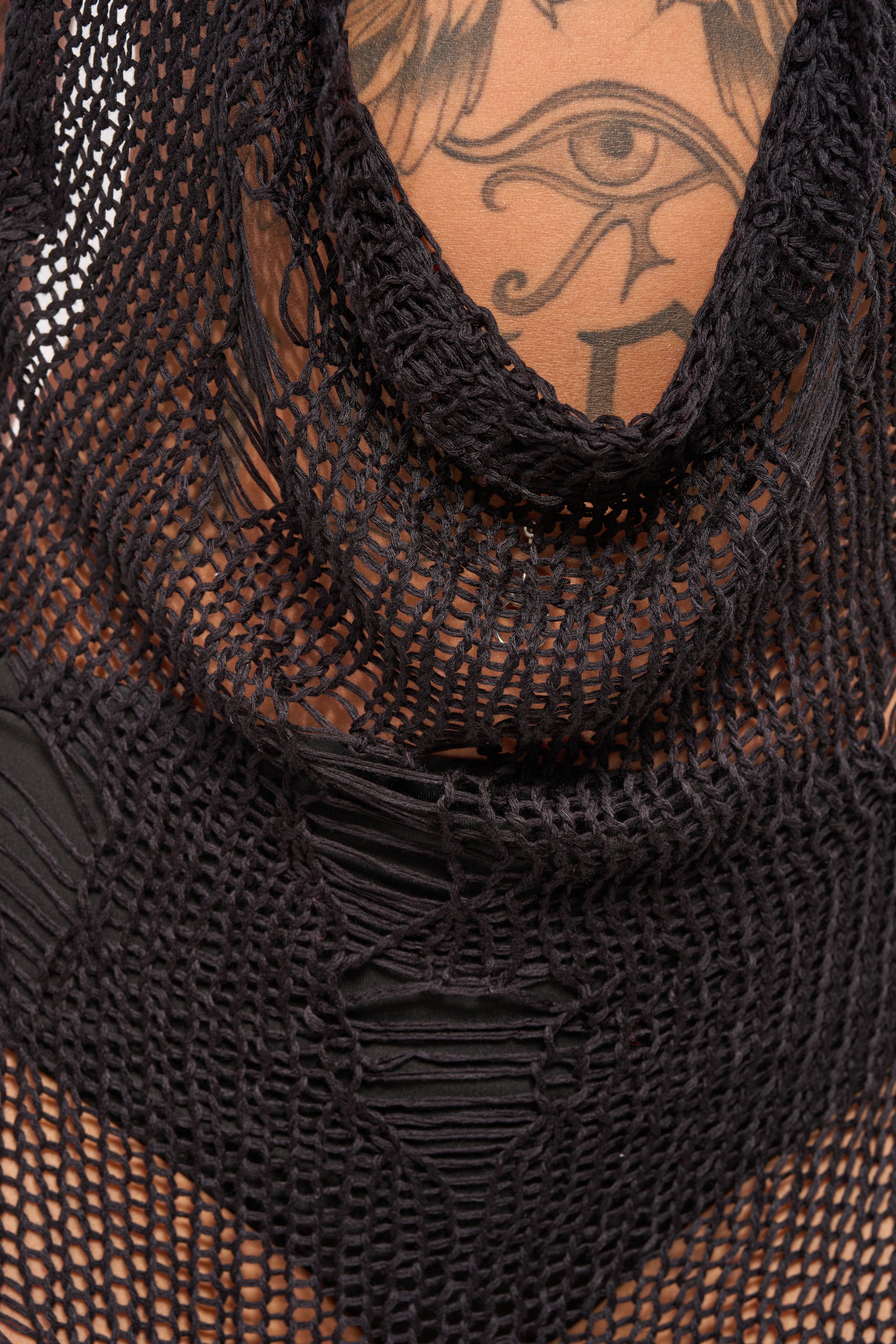 A close-up of a person wearing the MAKE A MESS KNIT MINI DRESS IN BLACK, showcasing an eye tattoo with decorative lines and shapes on their upper chest. 8