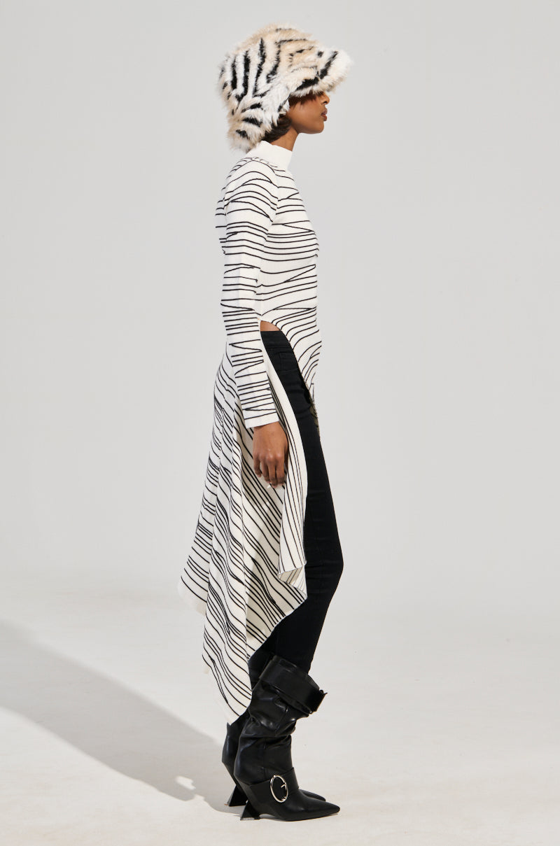 A person is wearing the ISA High Low Sexy Slit Striped Sweater in white, paired with black leggings and black ankle boots. They also have a matching striped hat and are standing in profile against a plain background.