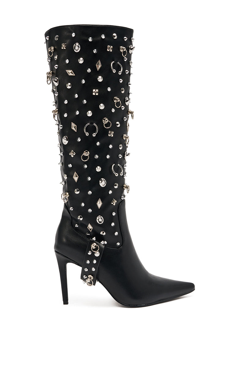 The AZALEA WANG AKRISTA BLACK HARDWARE EMBELLISHED STILETTO KNEE HIGH BOOT features luxe faux leather, a pointed toe, silver studs, rings, and jewels along the shaft, plus a metallic-accented strap at the ankle.