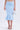 A person wears a light blue LUNA BANDAGE MIDI SKIRT in stretchy knit with a flared hem, silver strappy heels, and carries a metallic silver handbag against a plain white background.
