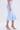 Someone wearing the LUNA BANDAGE MIDI SKIRT—a high-rise, knee-length mermaid silhouette in light blue bandage knit—paired with silver heels, stands against a plain light background.