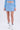 Wearing the ICY BLUE SPARKLE MINI SKIRT with a skater silhouette, a matching cropped cardigan, white frilly socks with black bows, and silver shoes, the person stands against a plain white background.