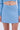 A person models the ICY BLUE SPARKLE MINI SKIRT in a skater silhouette with a matching long-sleeve top. Cropped from shoulders to mid-thighs, the image highlights the shimmering icy blue fabric and a visible belly button piercing.