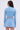 A woman with long, wavy brown hair is shown from the back wearing the ICY BLUE SPARKLE CARDIGAN and a matching pleated mini skirt. The background is plain and light-colored.