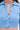 A close-up of a person wearing the ICY BLUE SPARKLE CARDIGAN, featuring a ribbed texture, collar, and four decorative crystal buttons, partially unbuttoned at the top to reveal their upper torso and part of their neck.