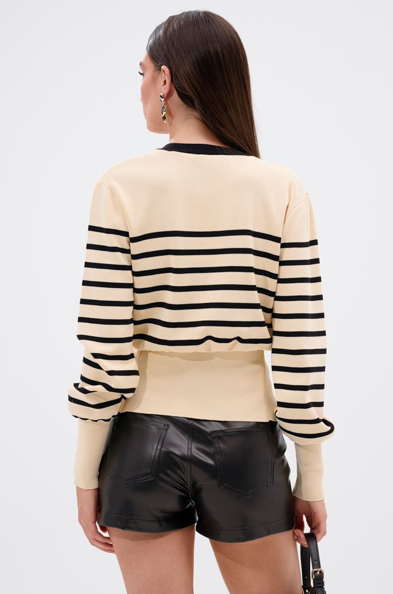 A woman with long brown hair, seen from the back, wears the REAL LIFE GOALS SWEATER with black leather shorts and holds a small black handbag against a plain light background. 4