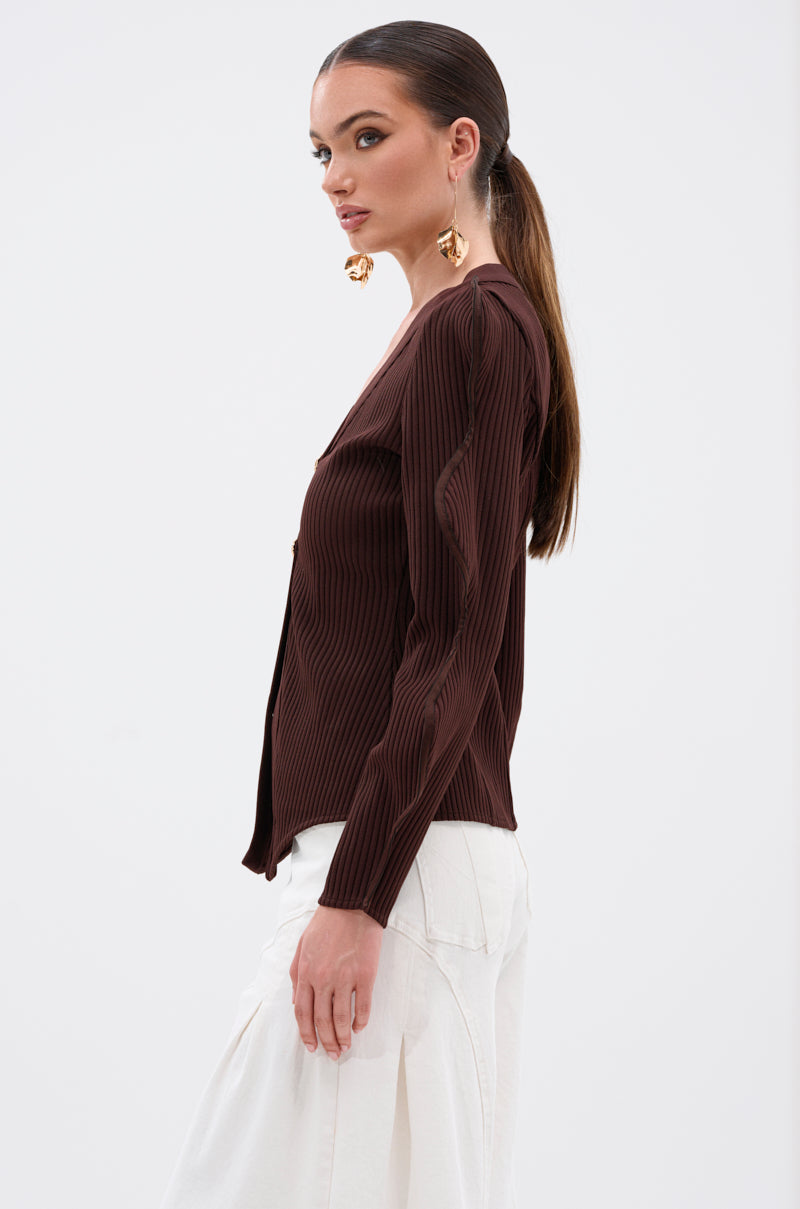 Woman in profile wears the DON'T ASK CARDIGAN—a ribbed stretch knit, long-sleeve brown top—with white pants and gold statement earrings, her brown hair tied back, standing against a plain white background. 3