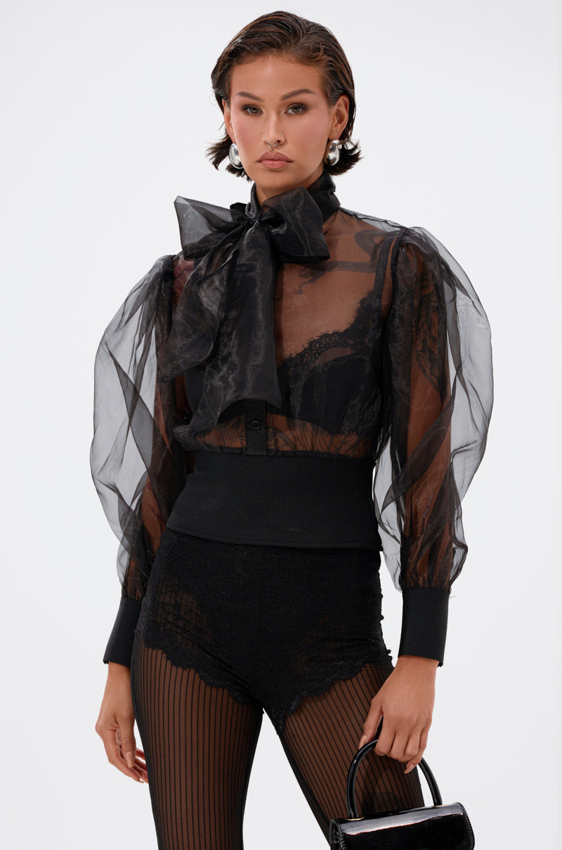 Wearing the DANCE AND SHAKE BLOUSE WITH BOW IN BLACK, paired with black lace shorts and striped tights, a person holds a small black handbag against a plain white background.