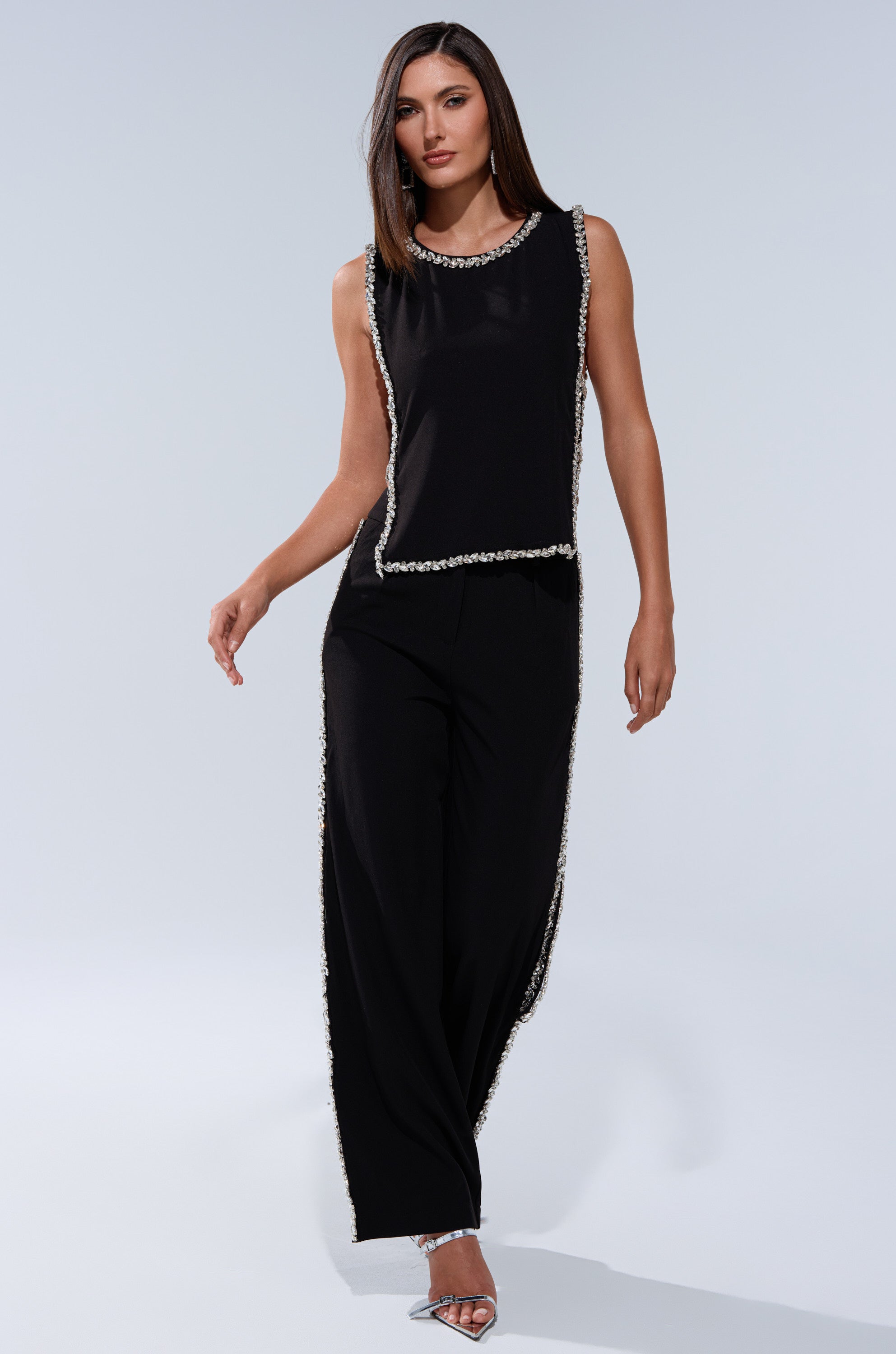 A woman in a TALK TO ME BABY BLOUSE WITH RHINESTONE and matching wide-leg pants poses confidently in silver high heels against a plain light grey background.