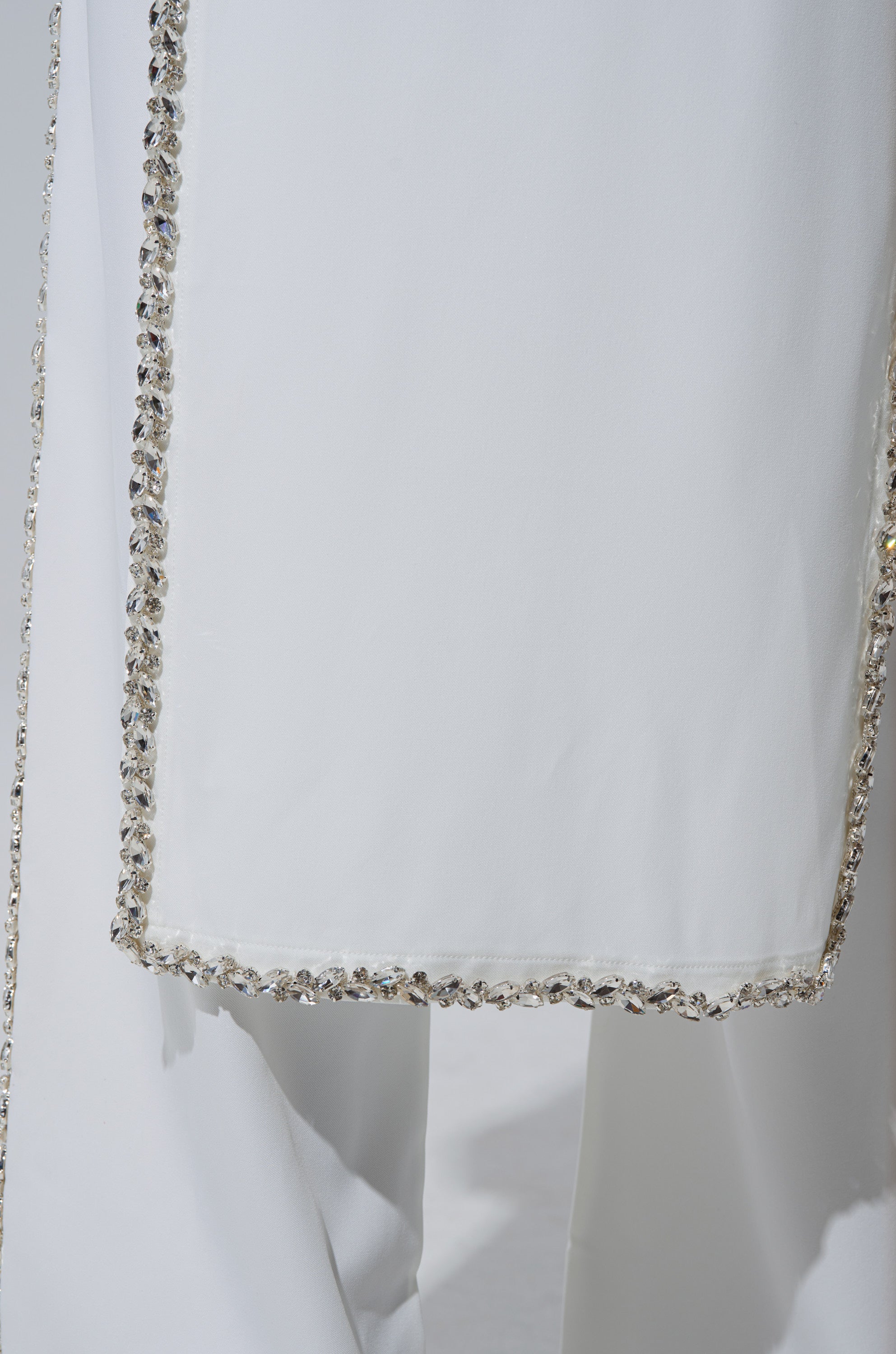 A close-up of the TALK TO ME BABY BLOUSE WITH RHINESTONE IN WHITE showcases its sleeveless design, smooth fabric, and a rectangular panel bordered with sparkling clear rhinestones for a chic, elegant look.