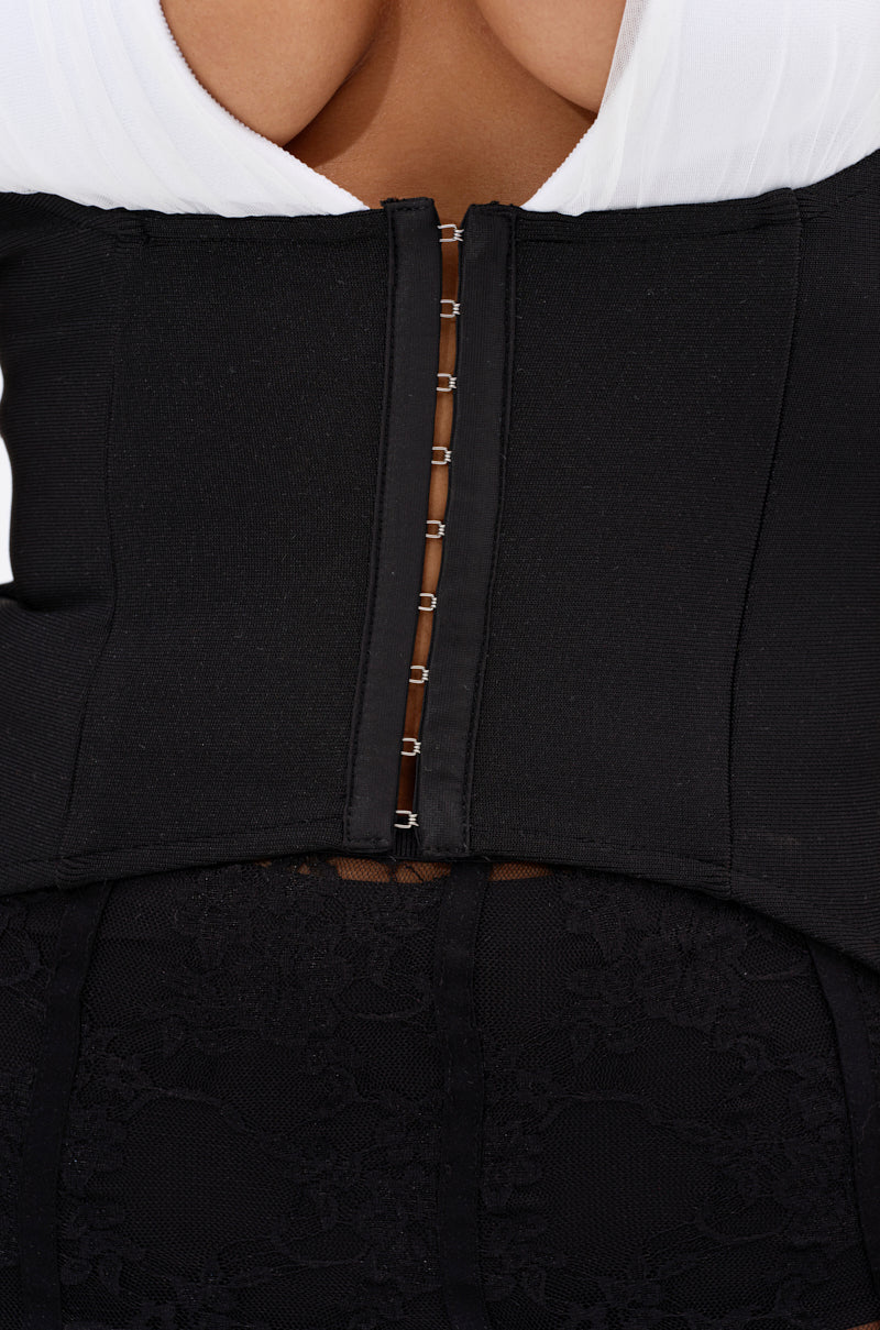 Close-up of a woman wearing the PRAIRIE GIRL CORSET TOP in black with hook-and-eye closures down the back, styled over white and paired with a black lace skirt for bold contrast. 6