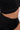 A close-up of a person’s midsection wearing the GINA SINGLE SHOULDER FRINGE TOP, a textured black stretch knit crop, paired with a high-waisted skirt, revealing part of their waist and tan skin.