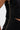 Close-up of a person wearing the GINA SINGLE SHOULDER FRINGE TOP, a textured black one-shoulder blouse with a prominent gold zipper down the side and a slight cutout detail near the waist.