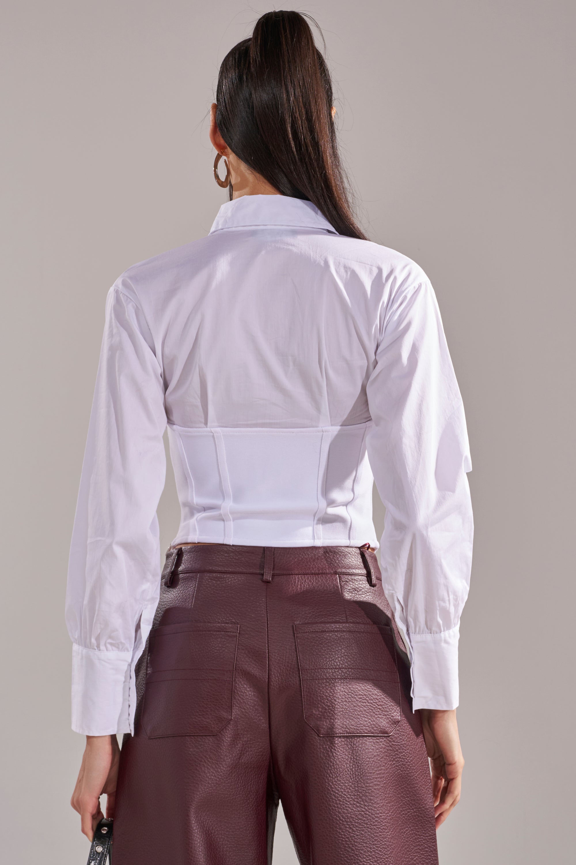 A person with long dark hair, wearing the SNATCHED UP CORSET TOP and high-waisted maroon faux leather pants, is shown from the back against a neutral background. 4