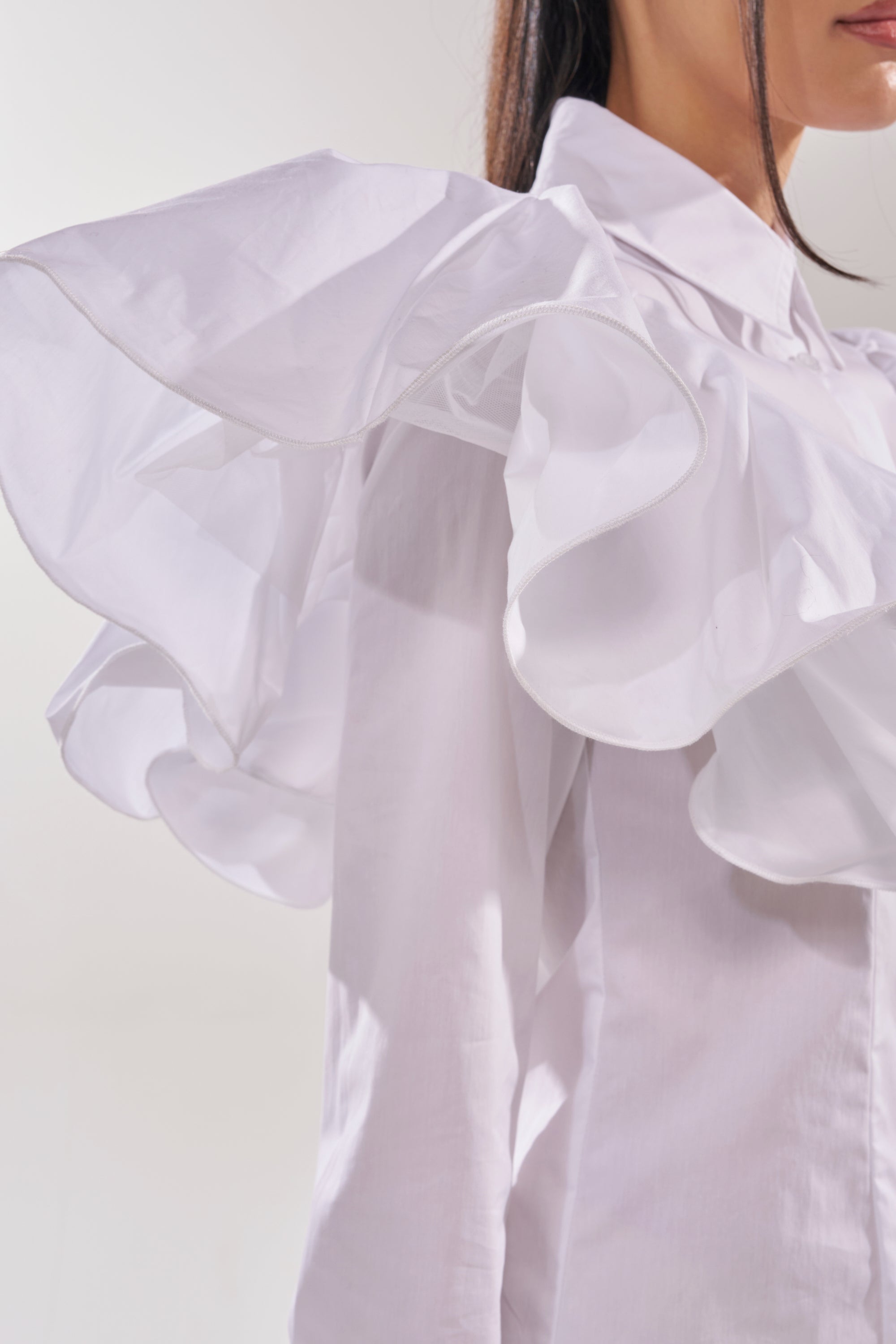 A woman wears the NO BIG DEAL BUTTON DOWN, featuring ruffle shoulders and dramatic sleeves. Only her lower face, neck, shoulder, and part of her arm are visible against a plain light background. 11