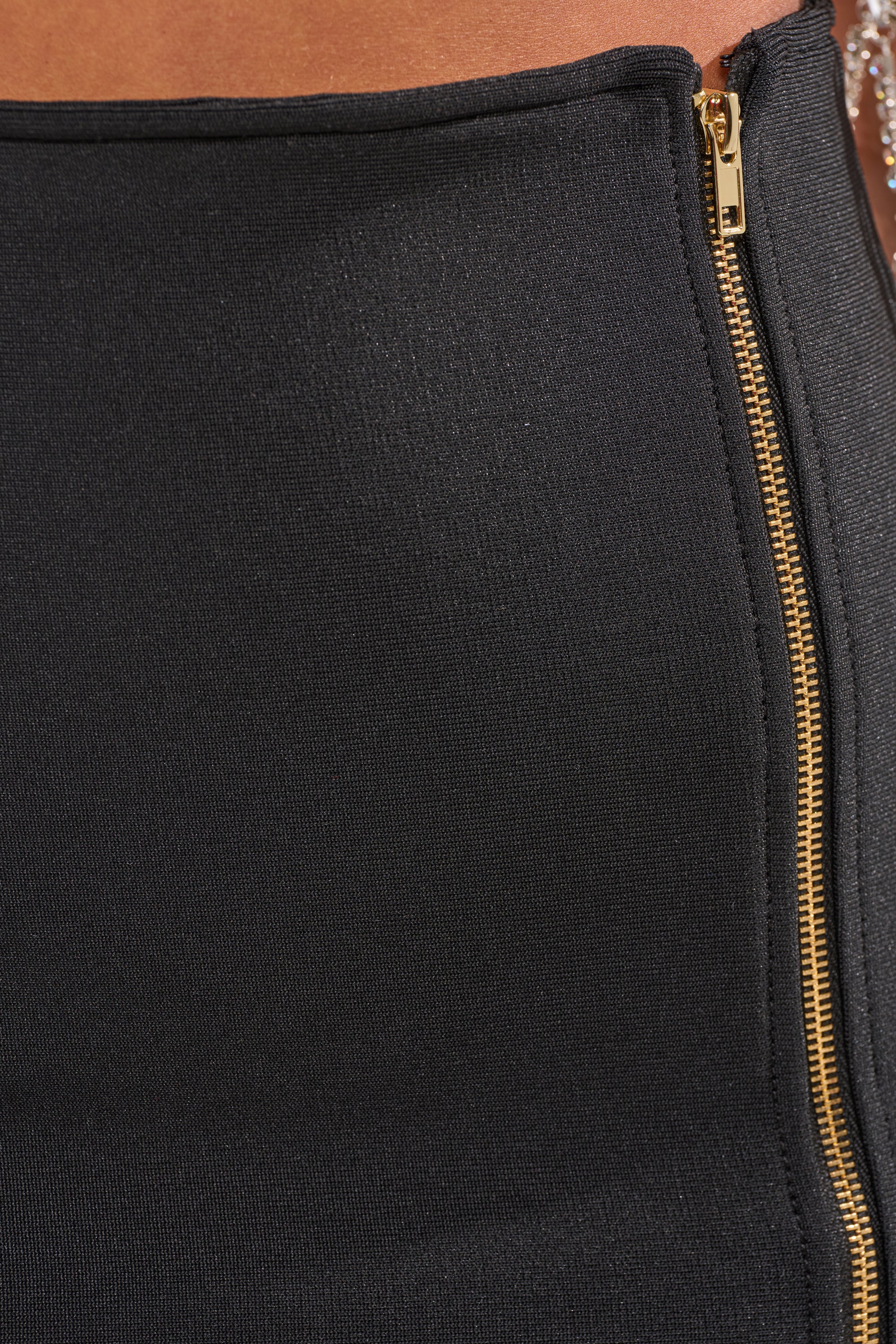Close-up of the UNZIP ME BANDAGE MAXI SKIRT in black, featuring a gold zip closure on the right side, a beaded strap detail, and a curve-hugging silhouette that reveals part of the midsection. 9