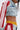 A person exudes street-style flair in the ALL AROUND THE WORLD AGAIN DENIM JACKET with red and white striped sleeves, paired with yellow elastic-waist shorts and matching striped shorts. Their face is partially visible and hair straight down.