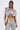 A woman embraces street style in the ALL AROUND THE WORLD AGAIN DENIM JACKET with red and yellow striped sleeves, matching jeans with colored panels, a white bralette, and small sunglasses against a plain background.