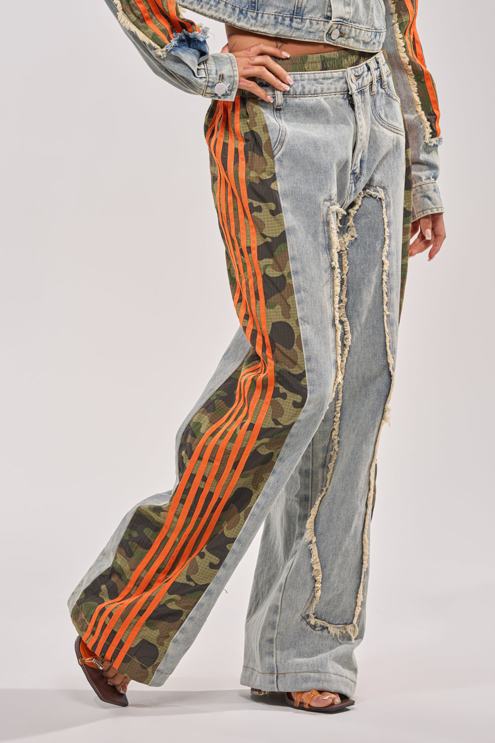 Wearing the ALL AROUND THE WORLD AGAIN RELAXED FIT DENIM pants with distressed patchwork, camo print, and bold orange side stripes, paired with open-toe heels and a cropped denim jacket creates a standout streetwear look. 3
