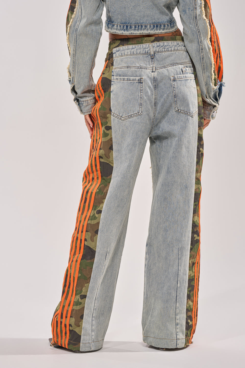 Someone wears the ALL AROUND THE WORLD AGAIN RELAXED FIT DENIM pants with orange stripes and a matching jacket. The back view photo shows off the bold mixed-material look and streetwear style. 5