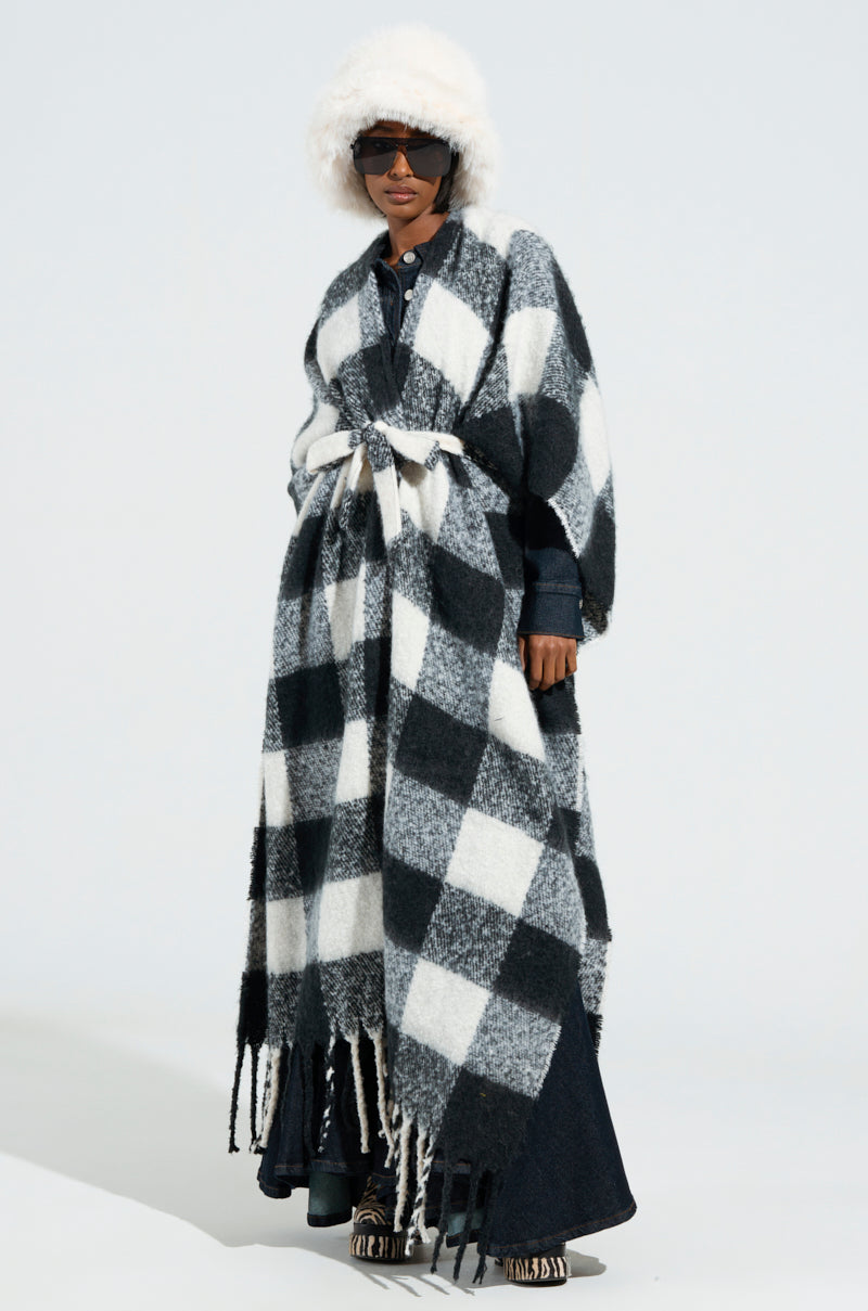 Set against a simple backdrop, an individual sports sunglasses and a furry white hat, elegantly styled in the CLASSY PLAID PONCHO adorned with chic fringe tassel detailing. The look is perfectly cinched at the waist with a white belt.